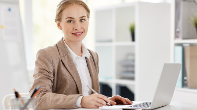 Secretária de governança sorrindo em ambiente corporativo, escrevendo em caderno ao lado de um notebook Secretária de governança sorrindo em ambiente corporativo, escrevendo em caderno ao lado de um notebook