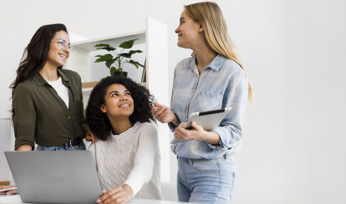 Three female nonprofit members collaborating with a tablet and laptop